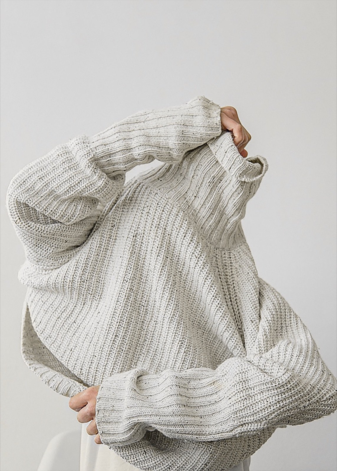 Person pulling a cream ribbed sweater over their head
